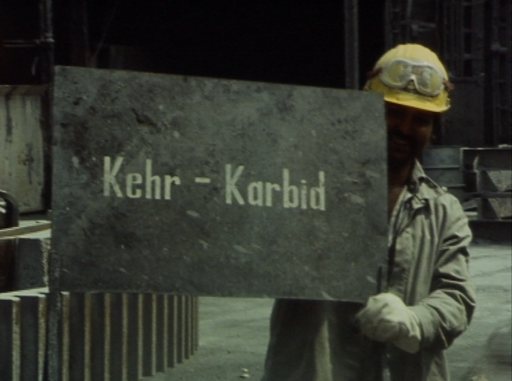 Filmfoto: Arbeiter mit Schild "Kehr-Karbid"